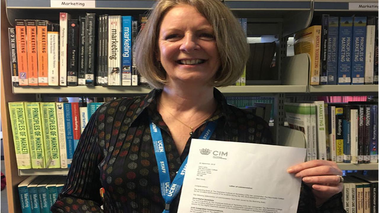 Tutor Carol Laing holding up a letter of commendation from CIM